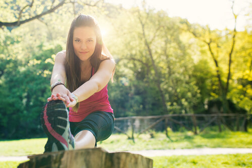 Woman stretching her leg on a log outdoors in a sunny park setting.