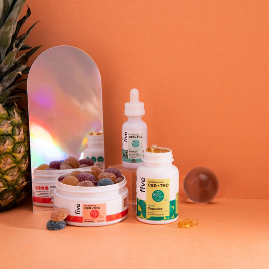 CBD + THC Full Spectrum gummies, capsules, and tincture bottles labeled "five" with a pineapple and a reflective mirror on an orange background