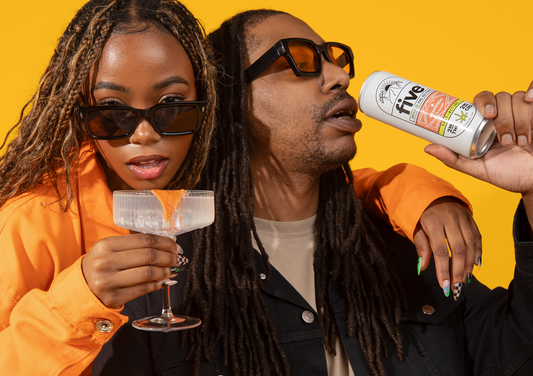 Two people wearing sunglasses, one holding a cocktail glass with an orange peel garnish, the other drinking from a can labeled 'five INFUSED THC SELTZER GRAPEFRUIT 2MG THC 2MG CBD FAST ACTING'.