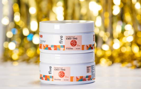 Front view of two stacked Five CBD+THC gummies jars showcasing product label and dosage on gold bokeh background